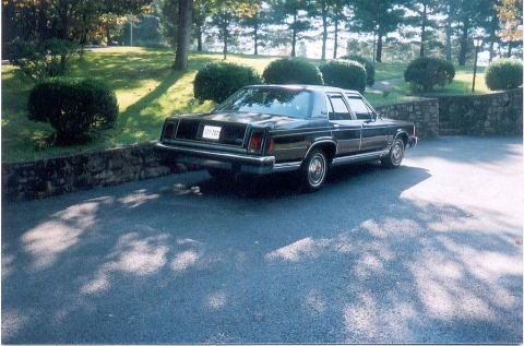 1982 Ford Crown Victoria LTD - This dark sedan is parked on a driveway with trees and bushes in the background.