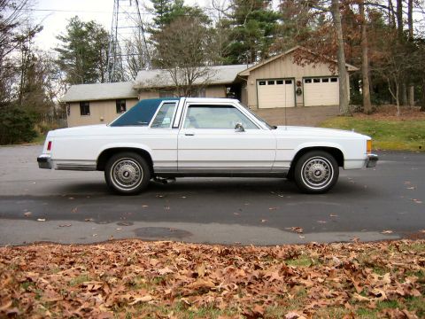 1985 Ford Crown Victoria LTD - Side view of a white 1985 Ford Crown Victoria LTD two-door sedan with a blue vinyl roof parked in front of a residential garage.