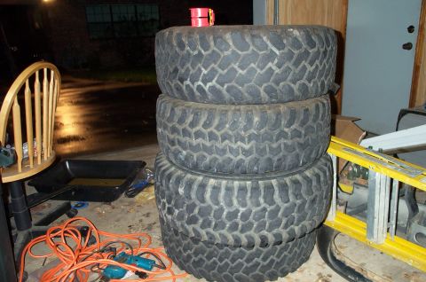 1978 Dodge Power Ram - Four off-road tires are stacked in a garage next to a ladder and tools.