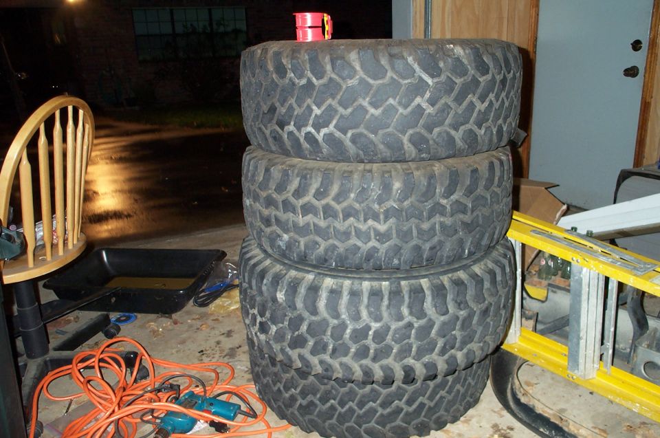 Stack of four large, knobby off-road tires with visible tread patterns