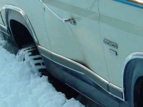 1986 Ford Bronco - A Ford Bronco XLT is partially submerged in snow, showing its side profile and chrome accents.