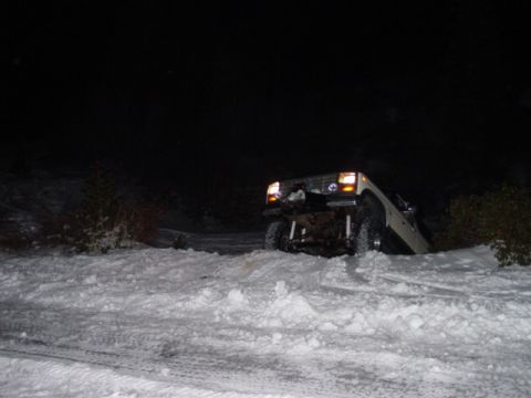 1986 Ford Bronco - A Jeep Cherokee XJ is stuck in a snowy area at night, with its headlights on.