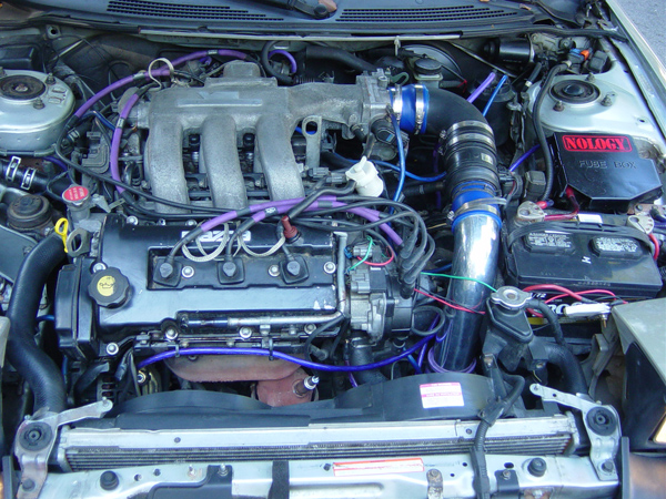 Engine bay with V6, black intake tube, blue coupler, purple plug wires