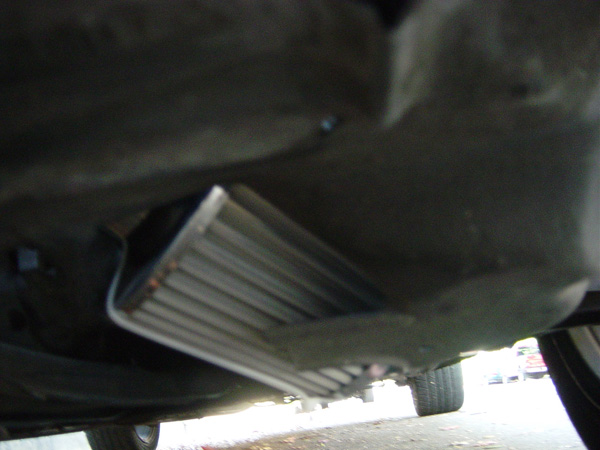 Finned aluminum cooler mounted low behind a front bumper, viewed from under the car