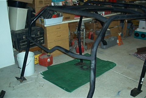 1986 Ford Bronco - A black roll cage is shown disassembled on a green tarp in a cluttered garage setting.