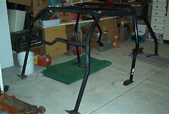 Black metal roll cage assembly on a concrete floor with a green tarp underneath
