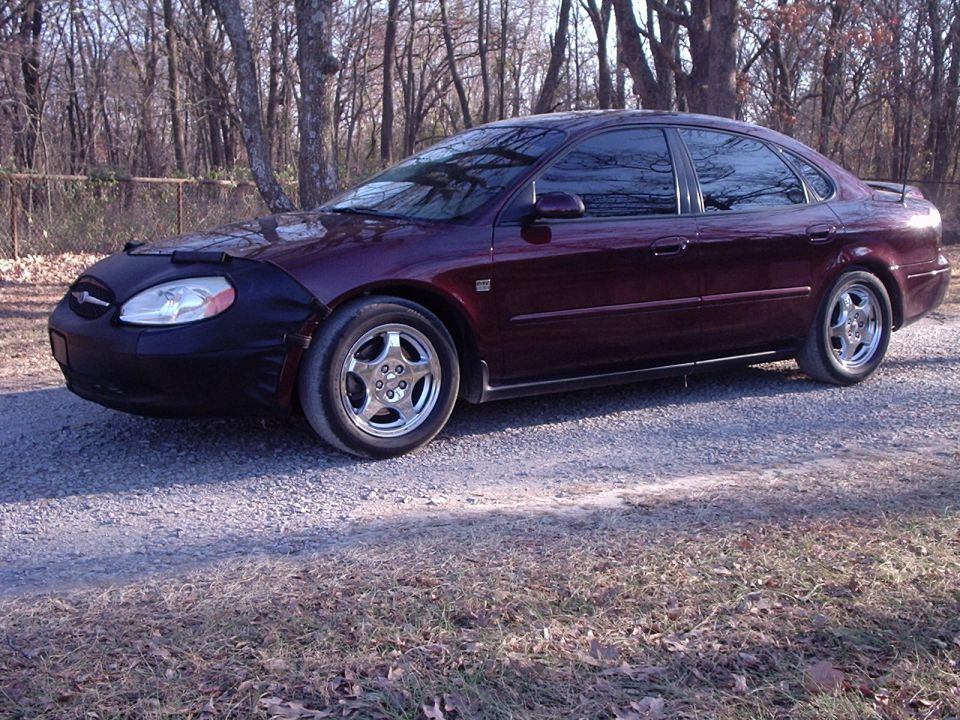 Maroon 2000 Ford Taurus with a car bra parked on a gravel road