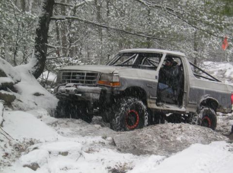 1995 Ford Bronco - A modified Ford Bronco navigates a snowy, rocky terrain with its doors removed.