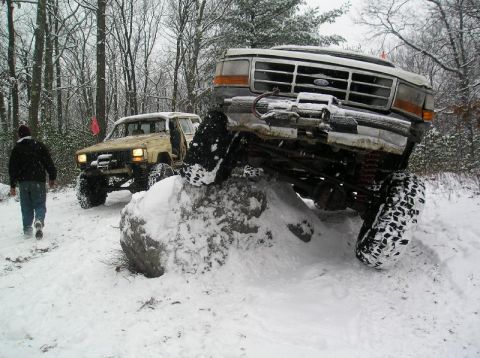 1995 Ford Bronco - Two off-road vehicles navigate a snowy trail, with one high-centered on a large rock.