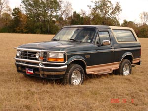 1995 Ford Bronco - This Ford Bronco is parked in a field with dry grass and trees in the background.