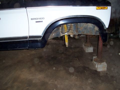 1983 Ford Bronco - 1983 Ford Bronco's front fender and suspension are visible while it's supported by blocks and stands.