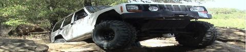 1986 Ford Bronco - A white Jeep Cherokee XJ is shown off-roading over large rocks.