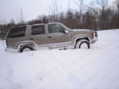 2000 Chevrolet Tahoe - This tan SUV is deeply embedded in snow, showing its side profile. The vehicle's body style suggests it is a 1995 model.