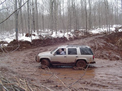 2000 Chevrolet Tahoe - A silver SUV navigates a challenging muddy path in a forest.