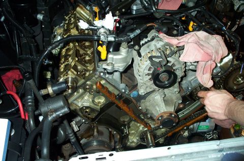 1998 Ford Crown Victoria - Close-up view of an engine's internal components, including the timing chain, with a mechanic's hands visible.