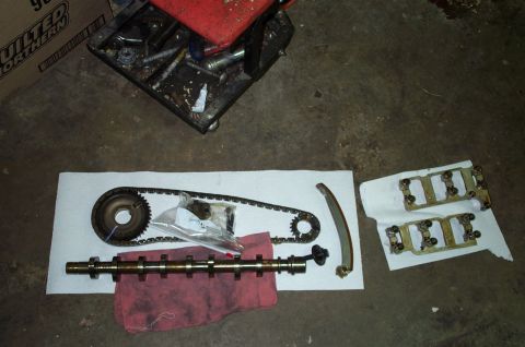 1998 Ford Crown Victoria - Engine timing components including a camshaft, timing chain, and valve train parts are displayed on a garage floor.