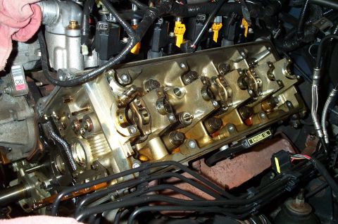1998 Ford Crown Victoria - Close-up view of an engine's valve train, showing rocker arms and yellow fuel injectors. An "ENGINE OIL" label is visible.