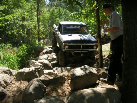 1977 Ford F-150 - A 1977 Ford F-150 tackles a challenging off-road course with large rocks and trees.
