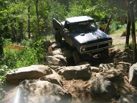 1977 Ford F-150 - This 1977 Ford F-150 is shown tackling a challenging off-road trail with large rocks and dense foliage.