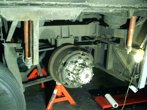 1979 Ford Bronco - Close-up view of a vehicle's undercarriage, focusing on a large brake drum assembly supported by orange jack stands.