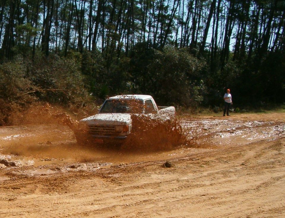 White pickup truck splashing mud, front view. A person stands in the background