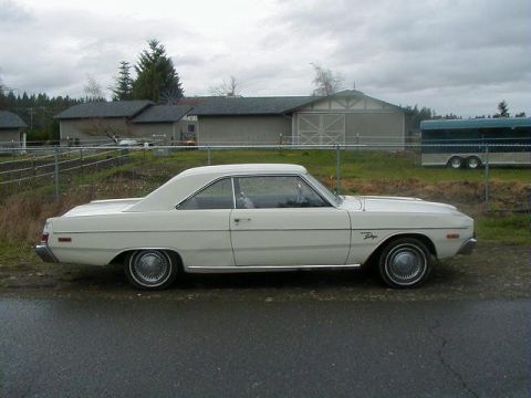 1993 Ford Bronco - A white coupe is parked on a wet asphalt surface with a fence and buildings in the background.