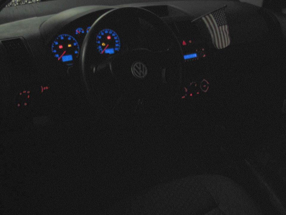 VW dashboard at night with lit blue gauges and steering wheel emblem