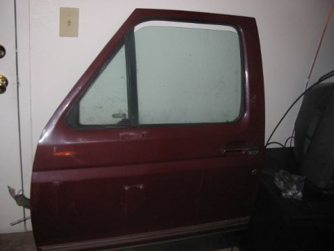 1991 Ford Bronco - Maroon car door with a triangular vent window and a chrome door handle, shown indoors.