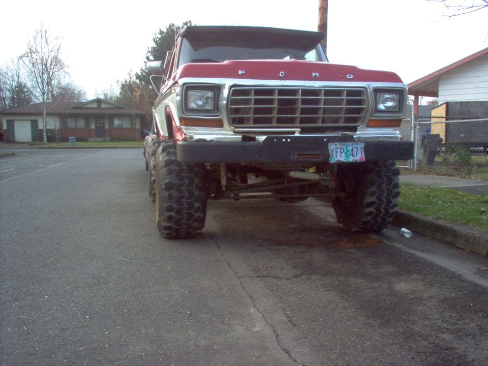 Front of lifted red/white Ford truck with big tires and chrome grille on a street.