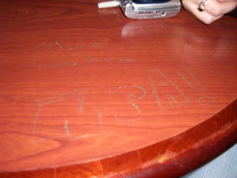 1996 Ford Probe - Scratched graffiti on a wooden table surface, with a cell phone and a hand in the background.