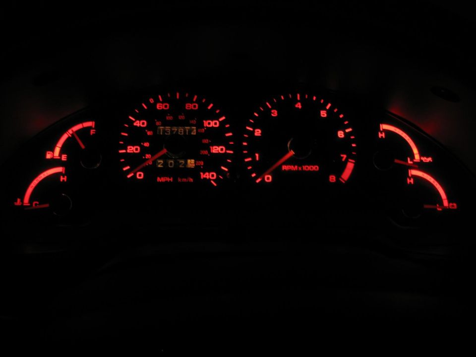 Red-backlit gauge cluster at night with speedometer, tachometer, fuel and temp gauges