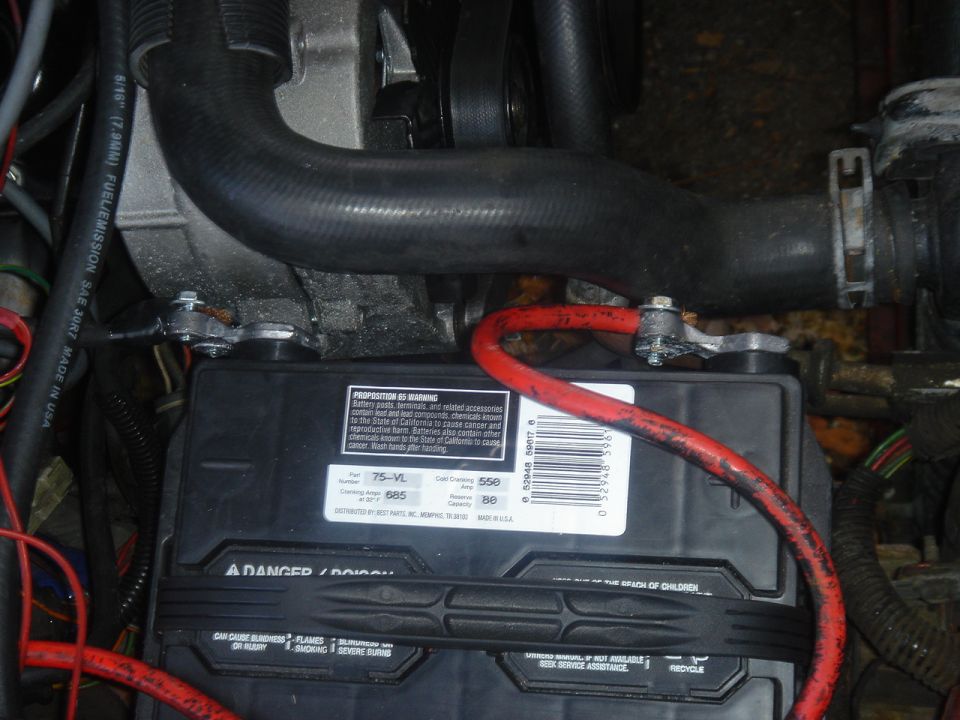 Car battery with red cables and engine hoses