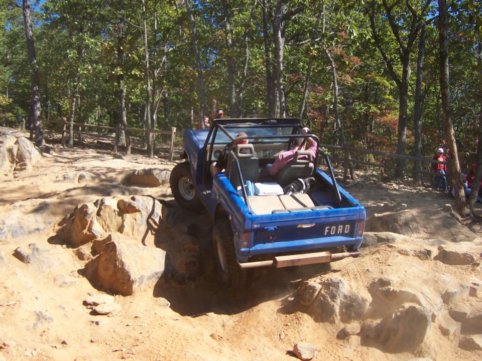Rear of topless blue early Ford Bronco on rocks at an off-road park, FORD on tailgate