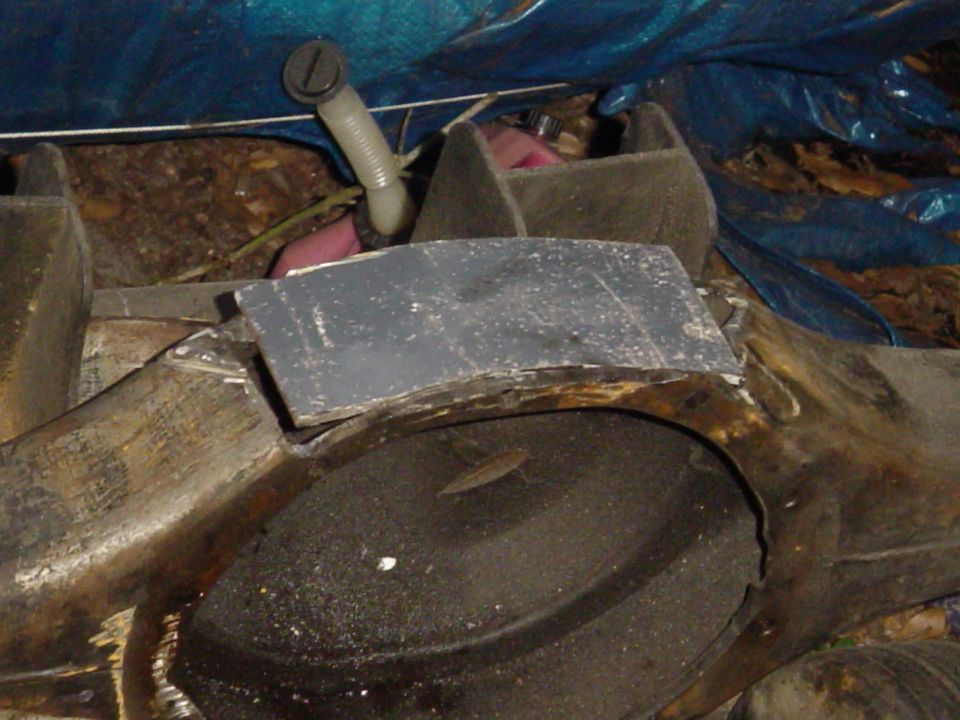 Close-up of a gray, curved metal piece over a dark, circular object, possibly a tire, under a blue tarp