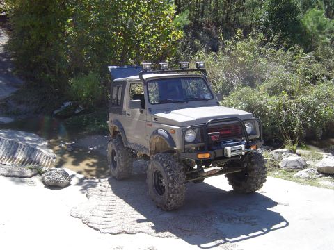1996 Jeep Cherokee - Modified Suzuki Samurai parked on a dirt path with trees and rocks in the background.