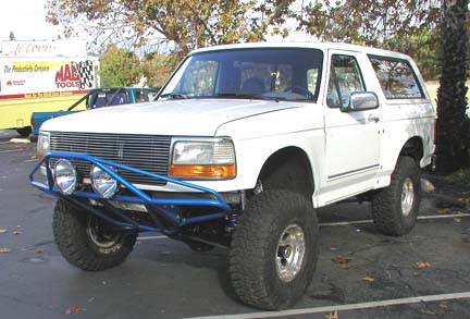 1984 Ford Bronco - White Ford Bronco with aftermarket blue bumper and large tires, front 3/4 view.
