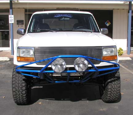 1984 Ford Bronco - Frontal view of a white SUV equipped with a custom blue off-road bumper and auxiliary lights.