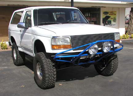 1984 Ford Bronco - White Ford Bronco with custom blue bumper and off-road tires. Likely a 1992-1996 model.