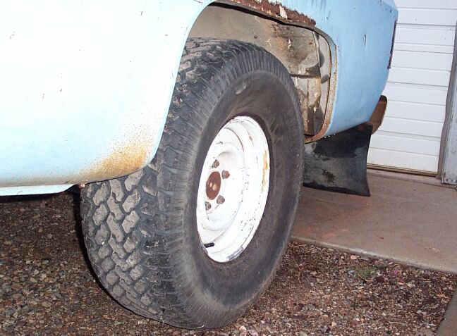 Front wheel of a faded light-blue pickup with white steel rim and rust on the fender
