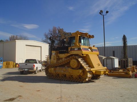 1966 International School Bus - Heavy equipment, a Caterpillar D9T bulldozer, is parked next to a pickup truck in front of a commercial building.