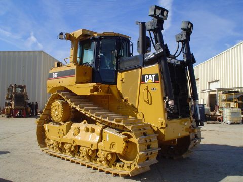 1966 International School Bus - A Caterpillar D9T bulldozer is shown from a three-quarter front view, with another piece of heavy machinery visible in the background.