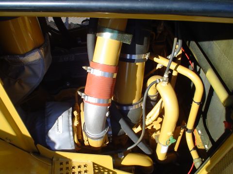 1966 International School Bus - Close-up of an engine compartment showing various hoses and pipes, including one with a red band and a bag with 'CATERPILLAR' visible.