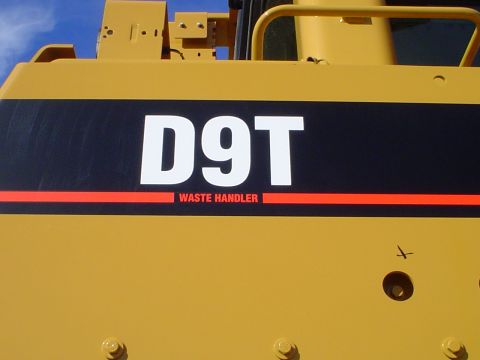 1966 International School Bus - Close-up of a yellow bulldozer's side panel, clearly displaying the 'D9T WASTE HANDLER' designation.
