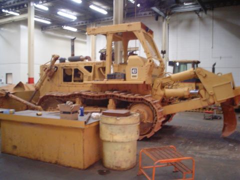 1966 International School Bus - A Caterpillar bulldozer sits in a workshop, with another machine in the background.
