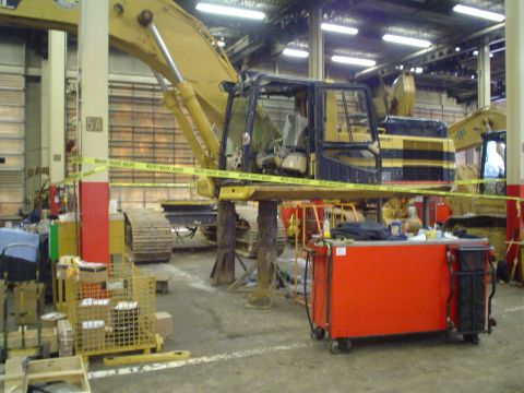 1966 International School Bus - An excavator is elevated on stands inside a workshop, with another machine visible in the background.