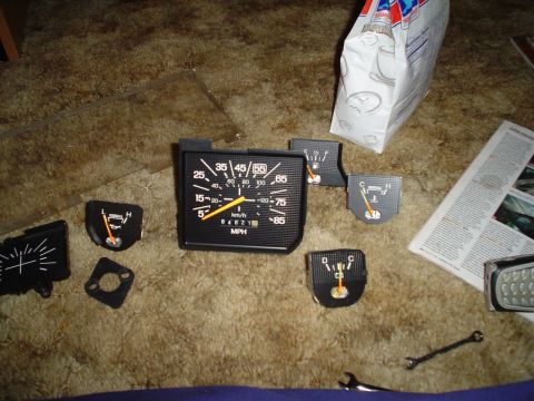 1984 Ford Bronco - A collection of automotive dashboard gauges, including a speedometer, fuel, and temperature indicators, are displayed on a carpeted floor.