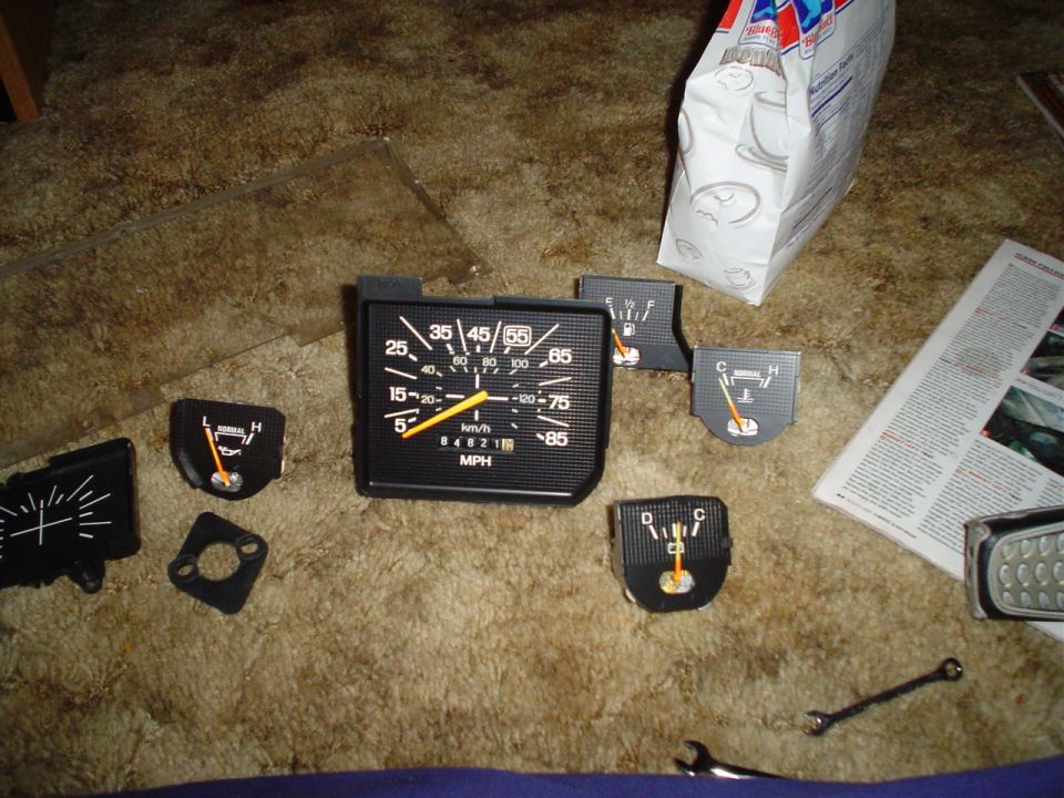 Dashboard gauges including a speedometer, fuel gauge, and temperature gauge laid out on a carpeted surface