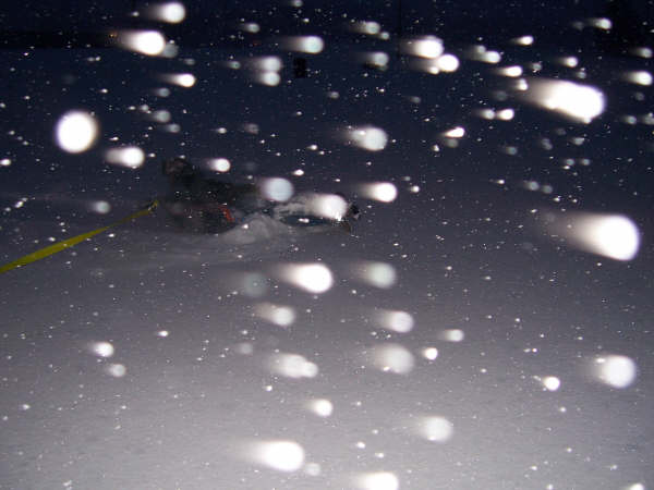 Vehicle driving through snow with lights on, possibly at night