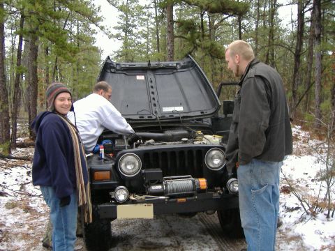 1997 Jeep TJ - Three people stand around a black Jeep Wrangler with its hood open in a wooded area with snow on the ground.
