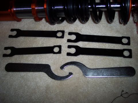 1995 Ford Probe - Adjustable coilover suspension components and associated wrenches are laid out on a carpeted surface.